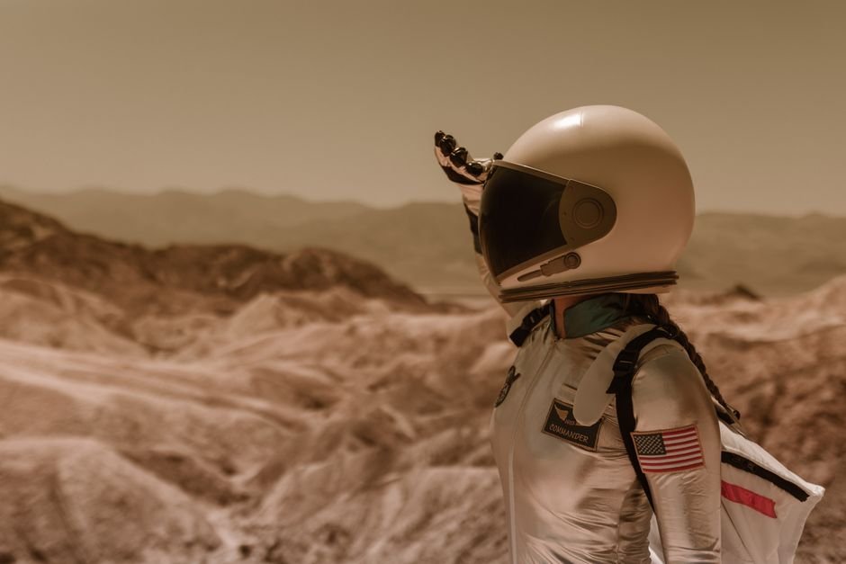 An astronaut in a space suit explores a desolate rocky landscape under a bright sky.
