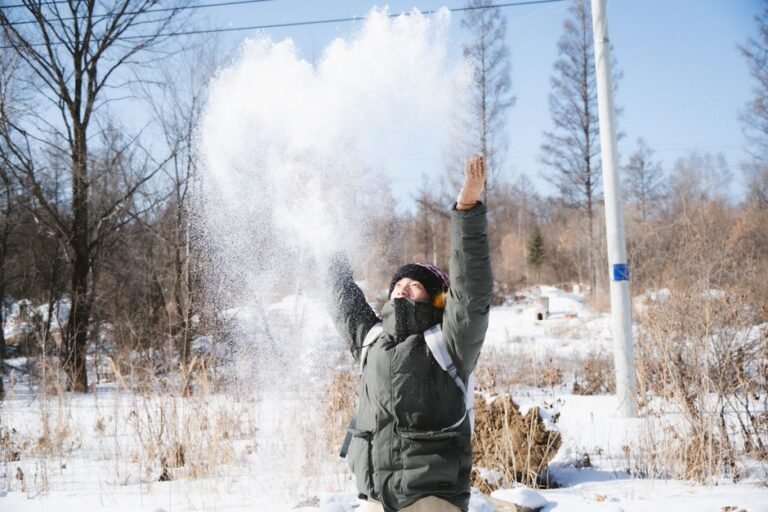 Person enjoying a sunny winter day, throwing snow in the air, surrounded by nature.