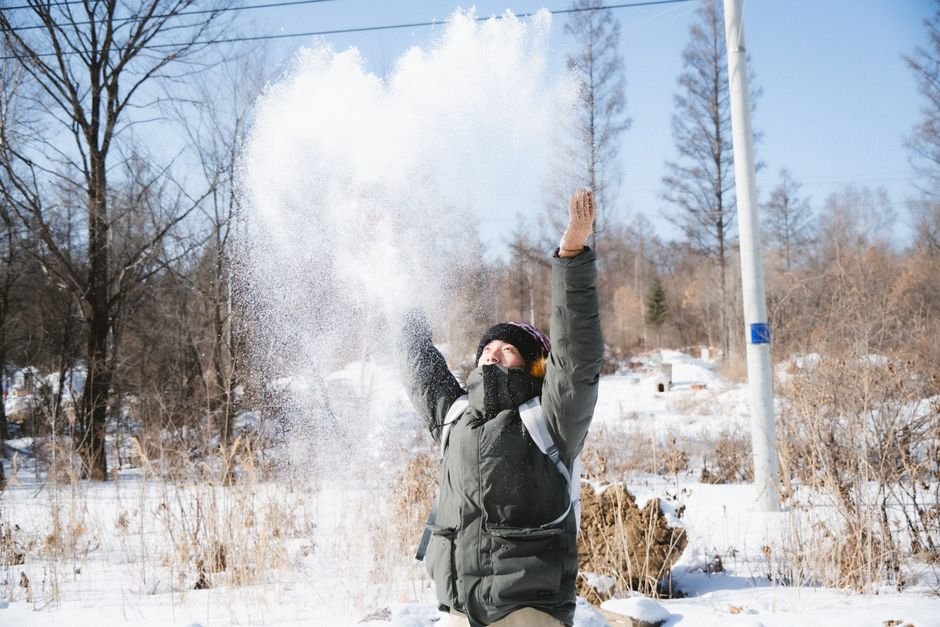 Person enjoying a sunny winter day, throwing snow in the air, surrounded by nature.