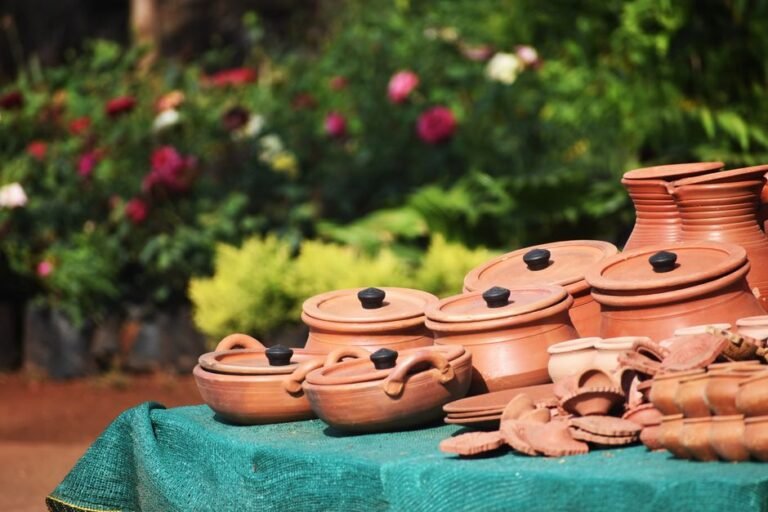 Collection of handmade terracotta pots and plates on display with garden background.