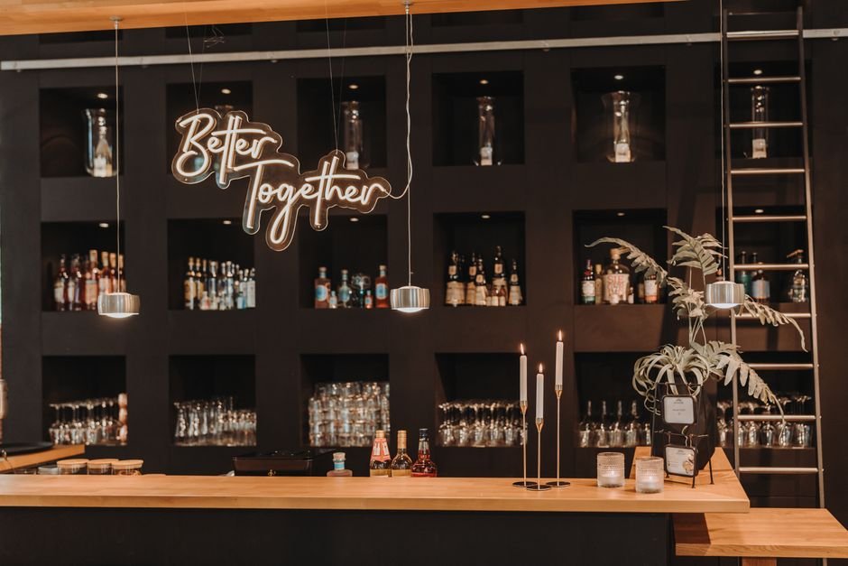 Stylish bar interior featuring a 'Better Together' sign, shelves of bottles, and glasses.