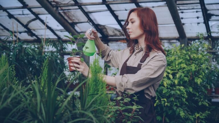 Female gardener spraying plants with water inside a greenhouse.