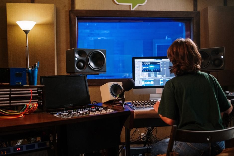 Back view of an audio engineer mixing sound in a recording studio with monitors and speakers.