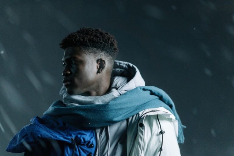 A young man in winter clothing looks away while standing in a snowstorm.