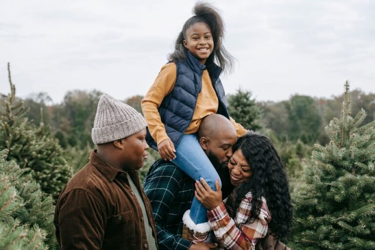 Happy African American family hugging and kissing in green lush spruce under cloudy gloomy sky