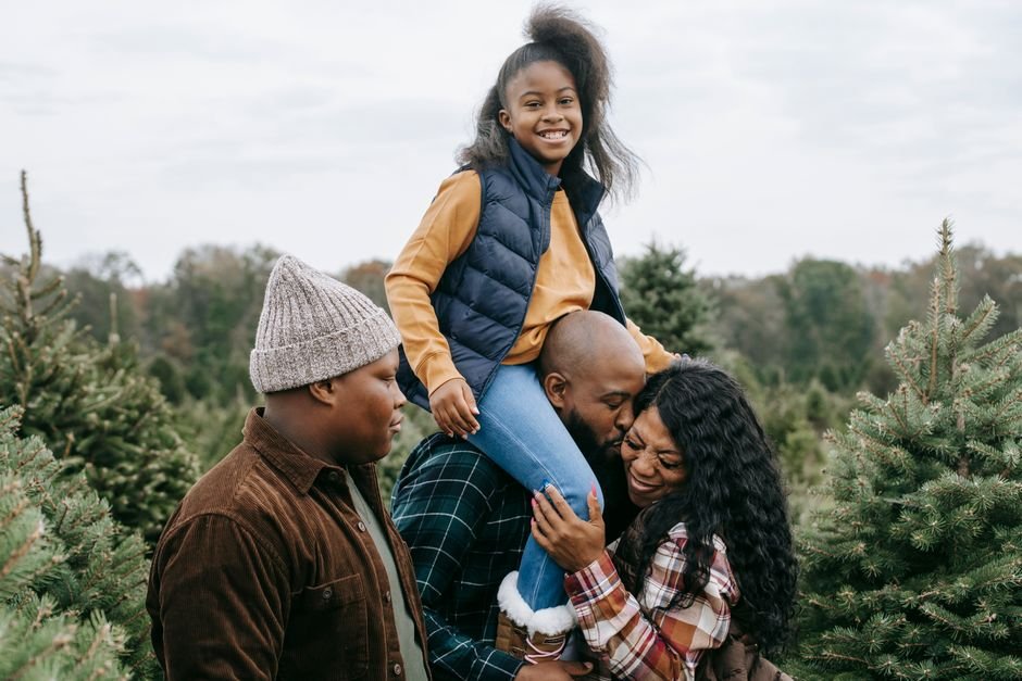 Happy African American family hugging and kissing in green lush spruce under cloudy gloomy sky