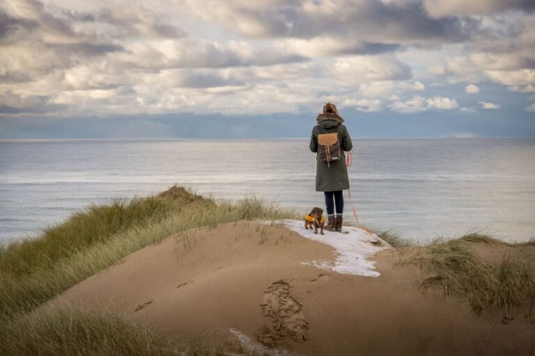 Woman with dog standing on scenic beach dunes in Agger, Denmark.