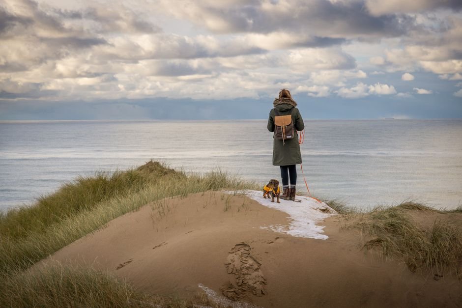 Woman with dog standing on scenic beach dunes in Agger, Denmark.