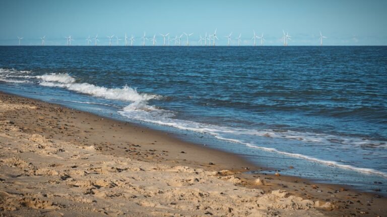 Idyllic Norfolk beach with serene waves and distant wind turbines under a clear sky.