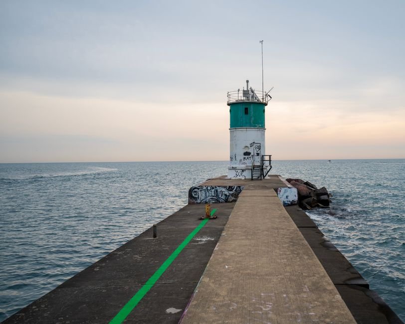 A tranquil scene of a lighthouse on a pier at sea during sunset, showcasing calm waters and serene sky.