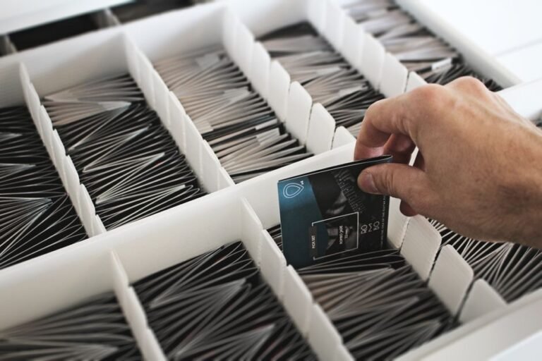 A hand selects a card from an array of organized cards in a white box.