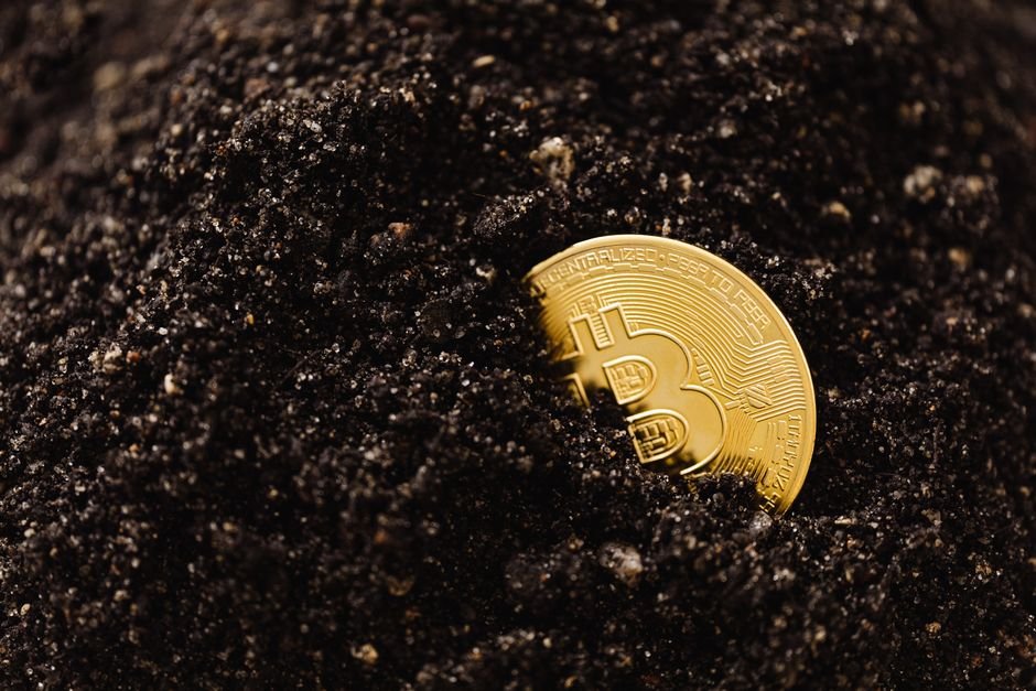 Golden Bitcoin partially buried in dark soil, symbolizing digital currency growth.